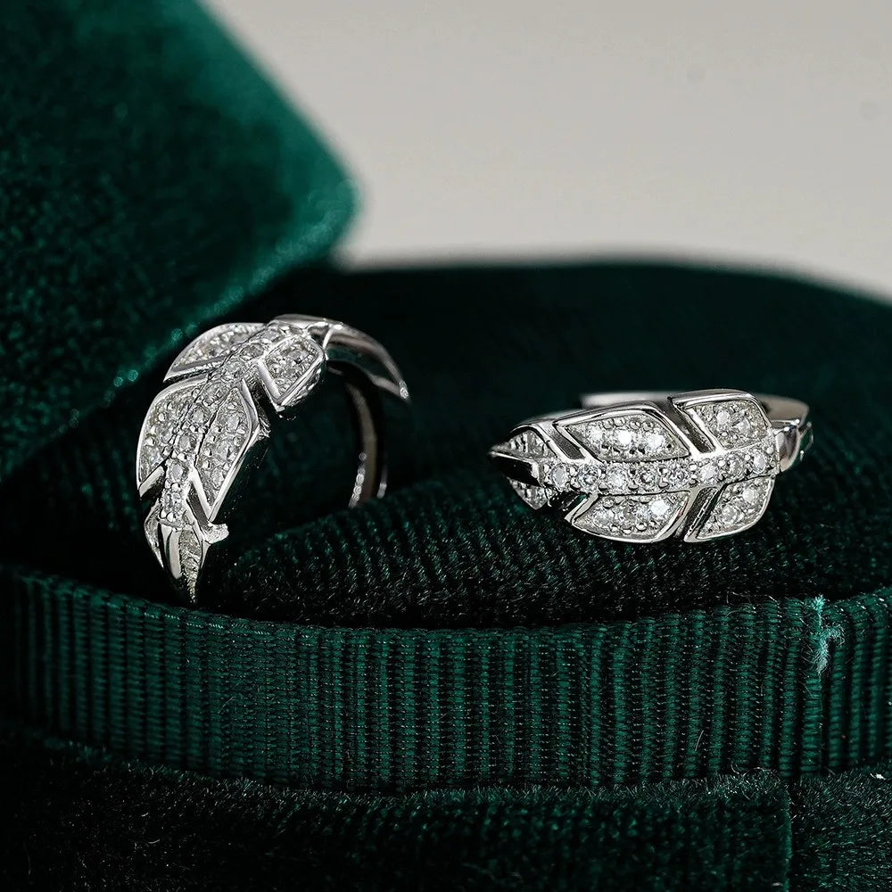 Two silver rings with feather designs on a green velvet surface
