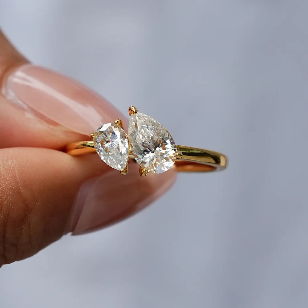 Gold ring with two pear-shaped diamonds held by a hand against a neutral background