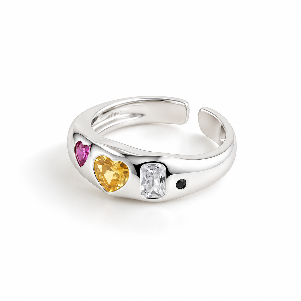 A silver adjustable ring featuring three heart-shaped gemstones in pink, yellow, and clear rectangular settings, with a small black heart detail, shown on a white background.